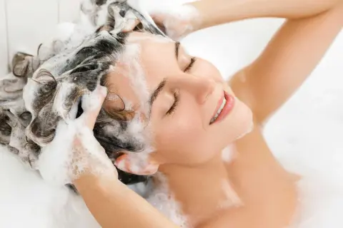 Donna con capelli schiumosi, ignara che l'ammonium lauryl sulfate fa male.