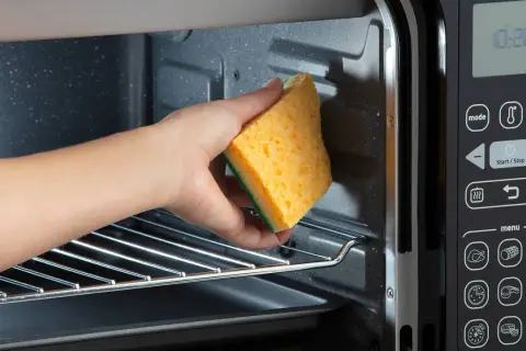 Mano che pulisce l'interno di un fornetto elettrico con una spugna gialla. Guida su come pulire il fornetto elettrico.