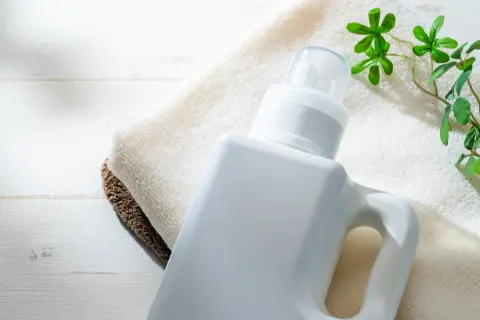 Flacone bianco di detersivi ecologici altroconsumo su asciugamani, con foglioline verdi.
