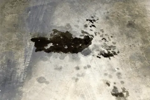 Macchie scure di grasso meccanico sul cemento, con tracce di pneumatici. Un problema comune da risolvere per chi lavora con i motori.