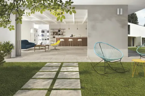 Modern patio with stone pavers, grass, and outdoor seating, opening to a bright, open-plan living and kitchen area.