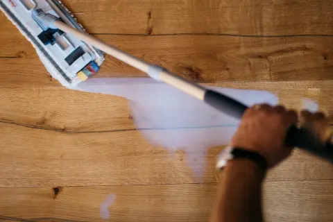 Mano che pulisce un pavimento in legno non trattato con uno straccio umido.