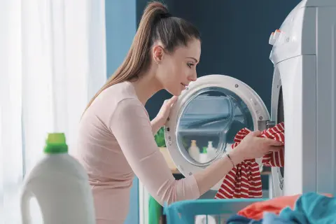 Donna carica la lavatrice, pensando a come la varechina cos'è e a come usarla per sbiancare i capi.