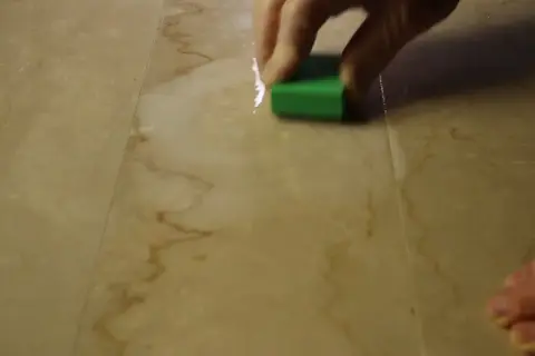 Mano che lucida un marmo corroso con una spugna verde.