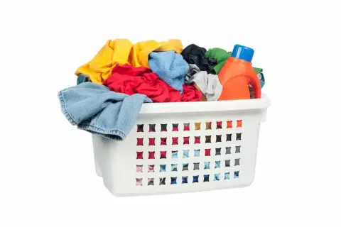 Cesto bianco pieno di panni colorati, con una bottiglia di detersivo arancione. Pronto per il bucato con perborato di sodio.