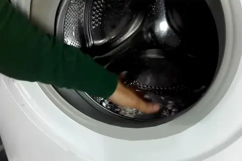 Mano che tocca l'acqua residua nel cestello della lavatrice, un passo per capire come togliere l'acqua dalla lavatrice.