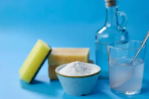 Spugna, sapone, bicarbonato e una bottiglia di aceto, ingredienti per un detersivo lavatrice fai da te.