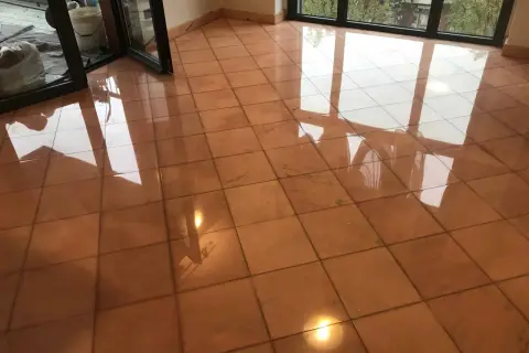 Pavimento in cotto lucido, riflessi di luce e finestre. Si intravede un secchio e sacchi, forse per pulire marmo con aceto.