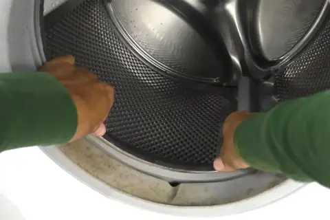 Mani che controllano il cestello lavatrice duro, con la sua superficie perforata e metallica.