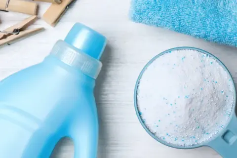 Detersivo in polvere in un misurino accanto a una bottiglia di detersivo liquido. Qual è meglio detersivo in polvere o liquido?