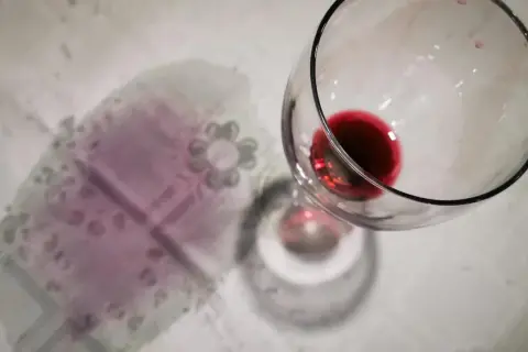 Un bicchiere rovesciato ha lasciato macchie di vino rosso sui capi colorati di una tovaglia.
