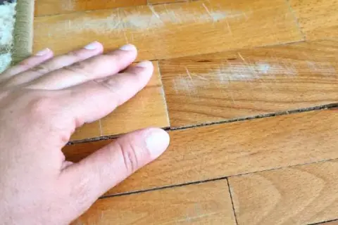 Mano sul parquet con macchie vecchie di olio e graffi evidenti.