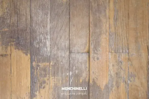 Parquet rovinato dall'acqua, con doghe in legno che mostrano macchie scure e usura, testimoni di un passato umido.