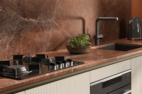 Piano cottura a gas su top in marmo rosso, con lavello nero, rubinetto moderno e bollitore Smeg. Le cucine con pavimento cotto hanno un fascino rustico.