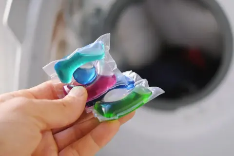 Mani che tengono capsule colorate per lavatrice. Attenzione, le capsule rovinano la lavatrice se usate impropriamente.