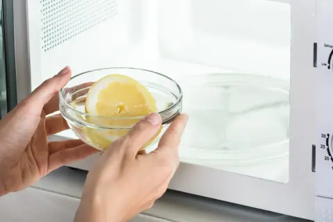 Mani inseriscono una ciotola con acqua e limone nel microonde, un metodo semplice per pulire l'elettrodomestico.