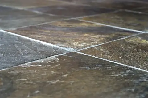 Primo piano di una pavimentazione in pietra di lavagna, con le sue venature naturali e le fughe bianche che creano un motivo geometrico.