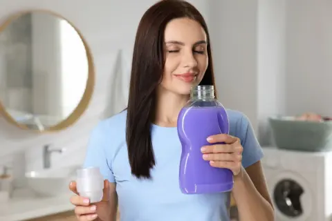 Donna annusa una bottiglia di ammorbidente viola, godendosi il profumo. Scopri come profumare la casa con l'ammorbidente.