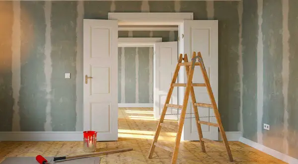 Rullo, secchio di vernice rossa e scala in legno pronti per togliere macchie di vernice secca dalle pareti di una stanza in ristrutturazione.
