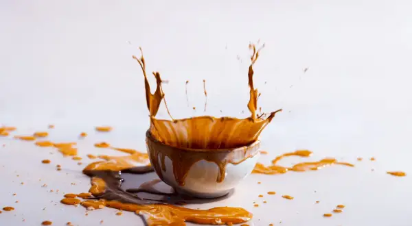Un caffè schizza da una tazza, creando un'onda liquida. Le macchie di caffè vanno via, lasciando una scia dorata sulla superficie bianca.