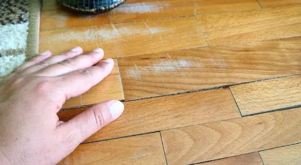 Mano su parquet graffiato, pronto per essere pulito con aceto e bicarbonato per un restauro fai-da-te.