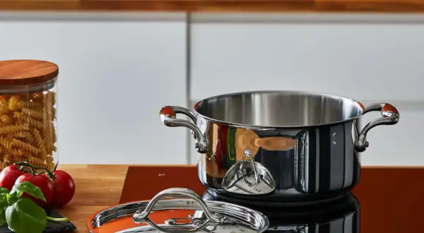 Pentola in acciaio lucido, coperchio e ingredienti freschi sul piano cottura. Scopri come pulire le pentole in acciaio per mantenerle splendenti.