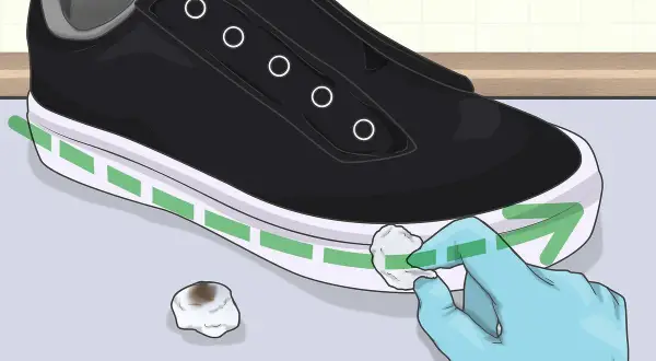 Guanto blu pulisce la suola bianca di una scarpa nera con un batuffolo di cotone. Ecco come pulire la suola delle scarpe per farle sembrare nuove.