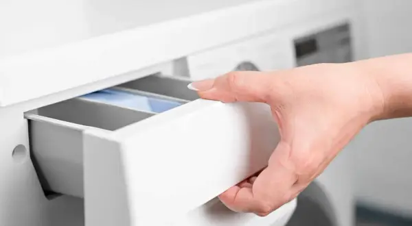 Mano inserisce cassetto lavatrice con percarbonato e candeggina.
