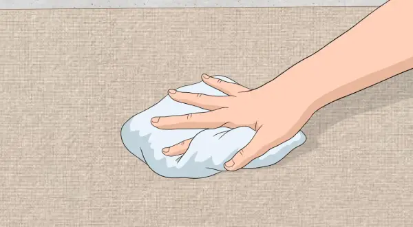 Mano che tampona una macchia su tessuto beige con un panno bianco. Guida su come togliere macchia d'olio.