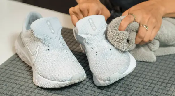 Hands cleaning light blue Nike sneakers with a grey cloth.