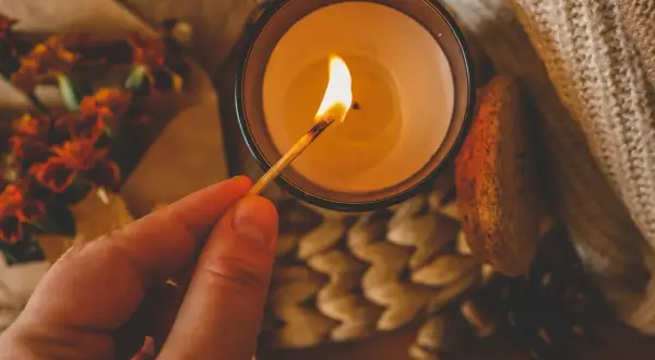Un fiammifero illumina una candela, un modo per spegnere le candele senza fare fumo. Atmosfera autunnale con fiori e zucca.