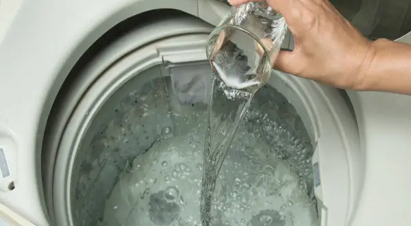 Mano versa liquido da un bicchiere nella lavatrice. Scopri quale aceto per lavatrice usare per un bucato impeccabile.