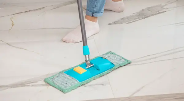 Piedi in calzini bianchi puliscono un pavimento in marmo con uno straccio blu e verde. Ecco come pulire il marmo per farlo brillare.