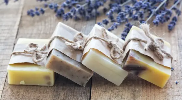 Saponi ecologici artigianali, avvolti in carta e legati con spago, su un tavolo di legno con fiori di lavanda.