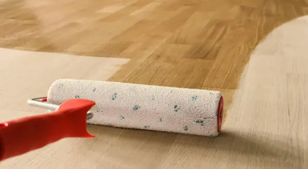 Rullo per verniciatura parquet in azione, che stende una mano di vernice su un pavimento in legno chiaro, creando un effetto bagnato e lucido.