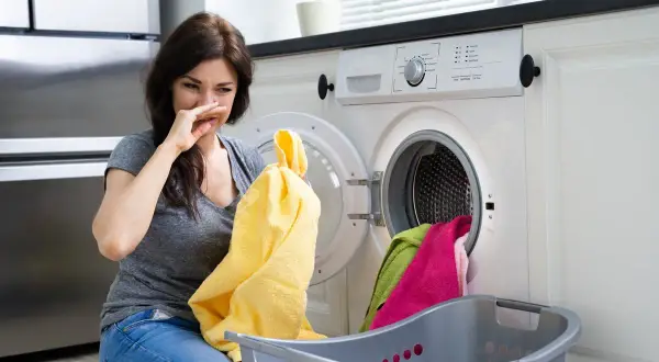 Donna con espressione disgustata annusa un panno giallo, i panni in lavatrice puzzano.
