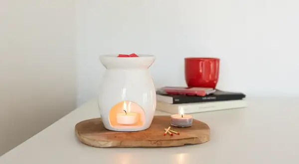 Diffusore bianco con candela accesa e cubetti di cera profumata sopra. Un'altra candela e fiammiferi completano la scena, mostrando che cos'è la cera per profumare l'ambiente.