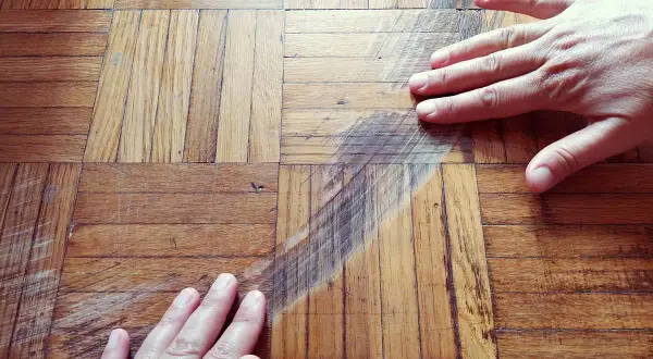 Mani sul parquet rovinato, graffi e segni evidenti. Si cerca una soluzione per pulire e ripristinare il legno.