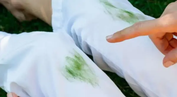 Un dito indica delle macchie d'erba su pantaloni bianchi, un piccolo disastro dopo una giornata all'aperto.