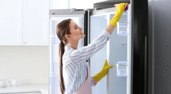 Donna con guanti gialli usa uno sgrassatore per pulire il frigo, rendendolo splendente.