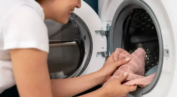 Donna sorride mentre mette un asciugamano rosa nella lavatrice, pronta per un bucato fresco.