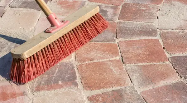 Una scopa con setole rosse su sanpietrini rossi e sabbia. Un modo semplice per capire come pulire i sanpietrini.