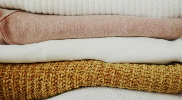 Pile di maglioni color pastello e ocra. Scopri come togliere elettricità dai vestiti per un comfort ottimale.