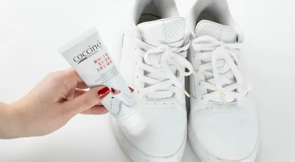 Mano con tubetto di crema per scarpe bianche, pronto a pulire le sneakers. Un metodo efficace per far tornare come nuove le tue scarpe bianche.