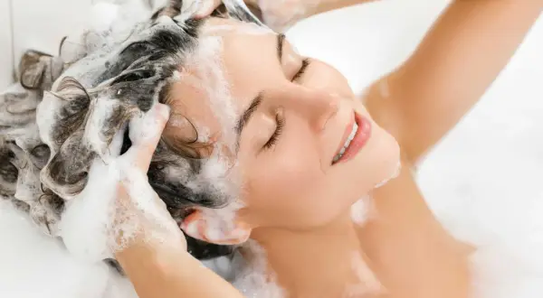 Donna con capelli schiumosi, ignara che l'ammonium lauryl sulfate fa male.