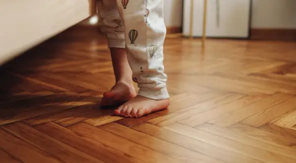 Bambino con pigiama a mongolfiere sui piedi nudi su un parquet lucido, pronto per scoprire come pulire il parquet dopo i lavori.