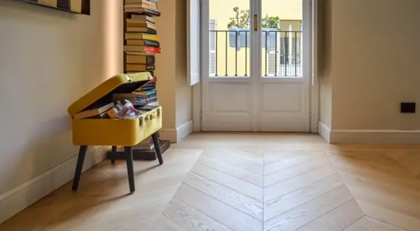Un elegante parquet a spina di pesce, con finitura opaca, riflette la luce che entra dalla porta-finestra.