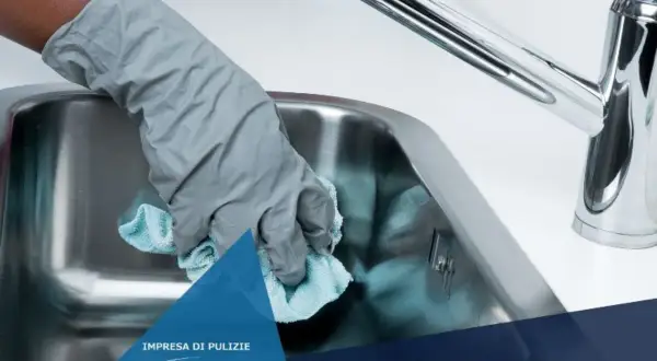 Mano con guanto grigio pulisce lavello in acciaio con panno azzurro. Scopri come pulire il lavello in acciaio dal calcare.