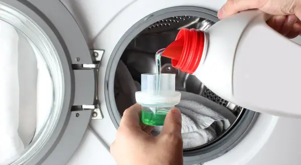 Versare il detersivo liquido nel tappo dosatore, un passo fondamentale per sapere come mettere la lavatrice e ottenere un bucato pulito.