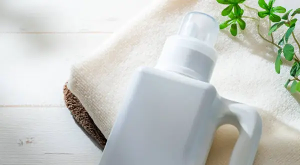 Flacone bianco di detersivi ecologici altroconsumo su asciugamani, con foglioline verdi.